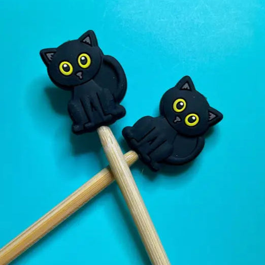 Two black cat-shaped stoppers on wooden knitting needles against a blue background
