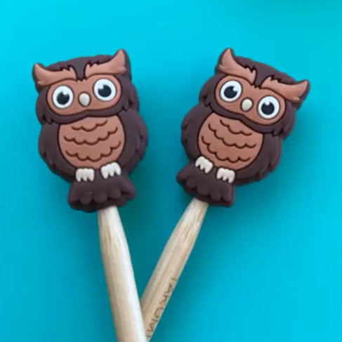 Two owl-shaped pont protectors on the tips of two light brown needles on a blue background